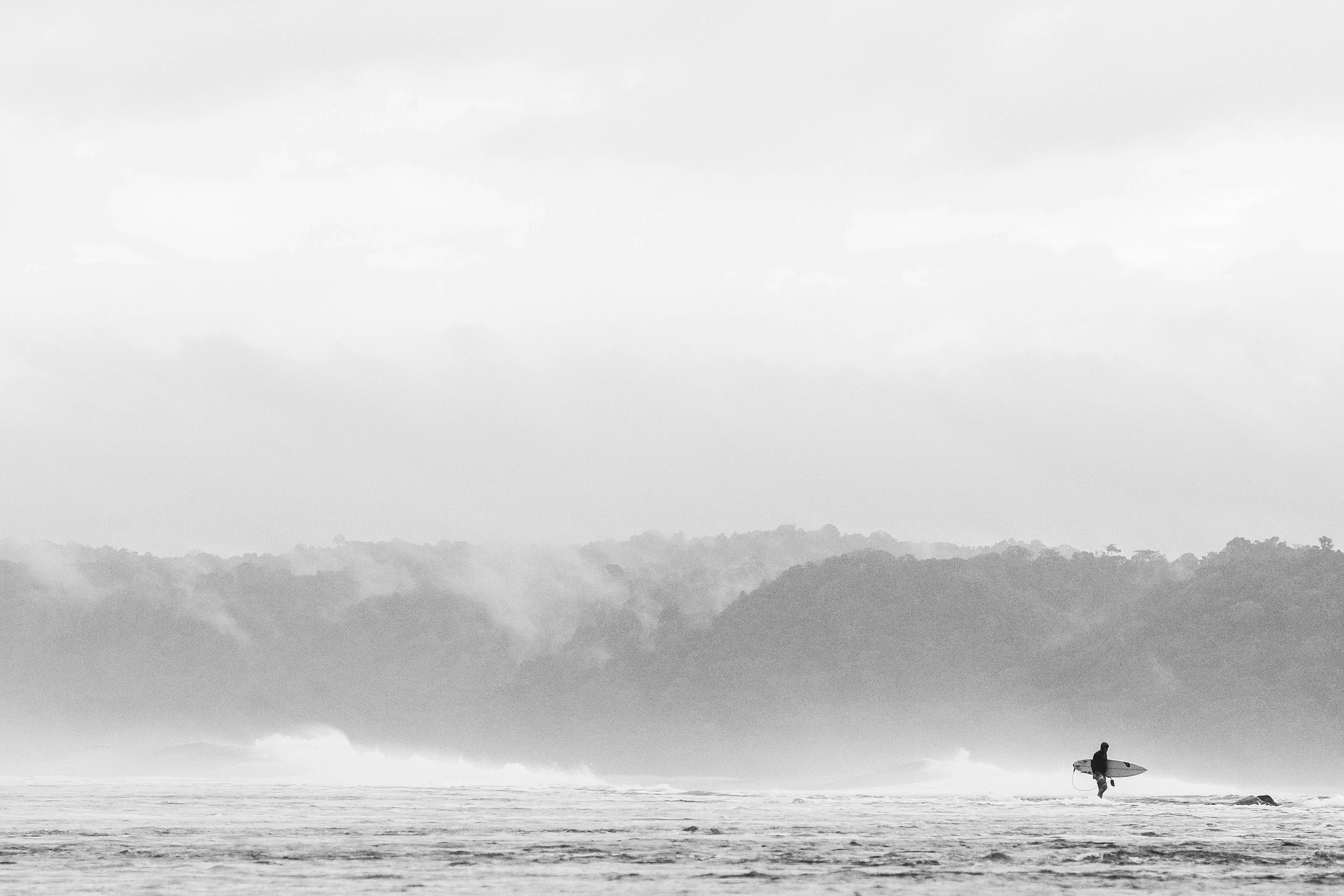 person carrying surfboard standing on the water during daytime photography